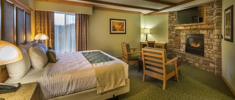 A hotel room with a bed, a desk, a chair, a fireplace, and a television.