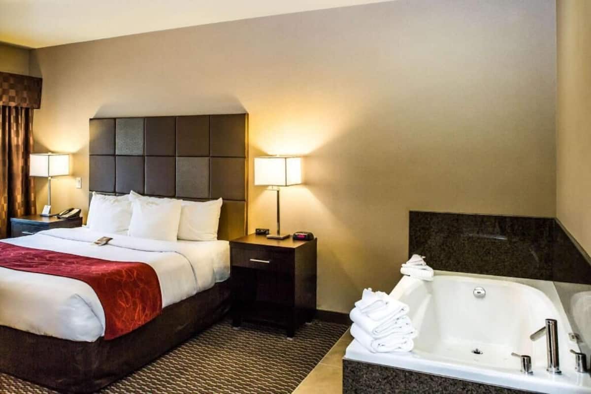 A hotel room with a bed, bedside tables, lamps, a bathroom with a bathtub, and a shower.
