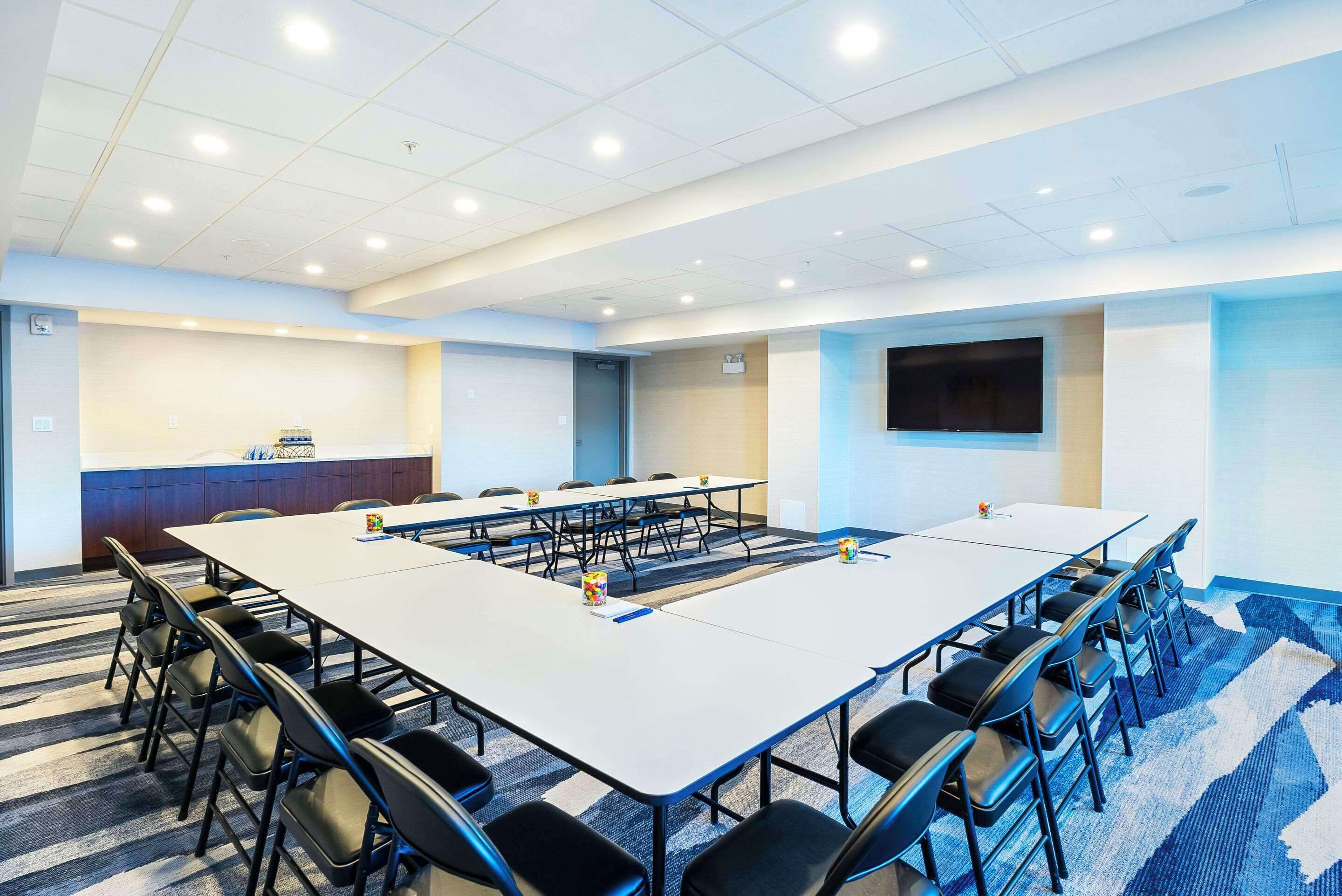 Un salón de conferencias con una larga mesa, sillas, una pantalla de televisión y una zona de recepción.