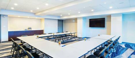 Un salón de conferencias con una larga mesa, sillas, una pantalla de televisión y una zona de recepción.