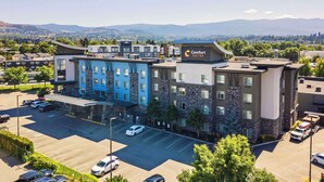 Un hotel de diseño moderno, con un llamativo letrero de 'Comfort Suites'. Cuenta con un estacionamiento con varios coches y vistas a montañas distantes.