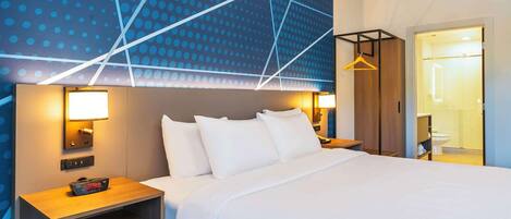 A modern hotel room with a large bed, bedside tables, a nightstand, and a wall with geometric patterns.