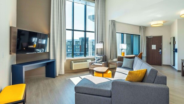 Una habitación de hotel moderna con un ventanal grande, un televisor de pantalla plana, un sofá, una mesita y una silla.