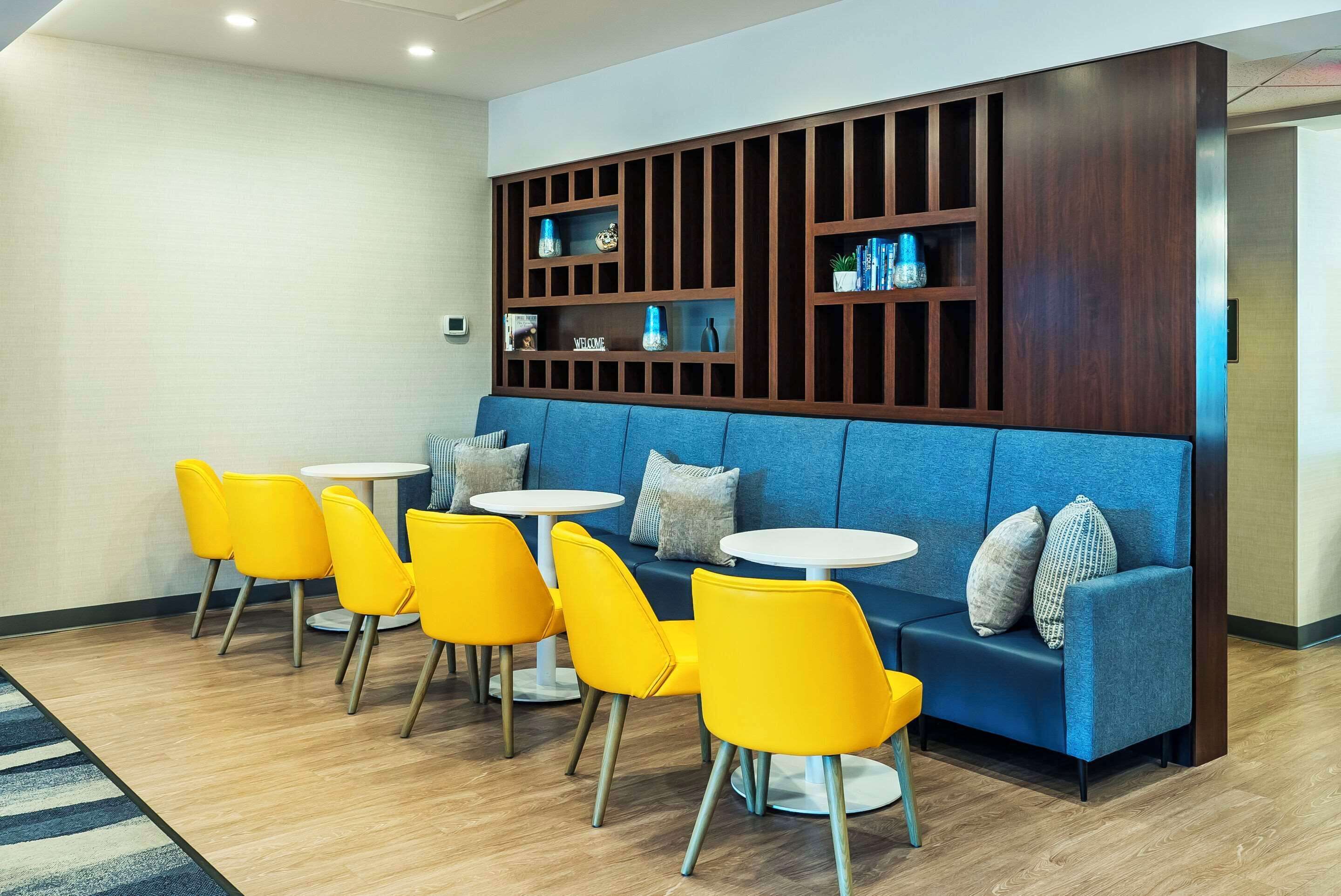 A modern lounge area with a blue sofa, yellow chairs, and white tables.