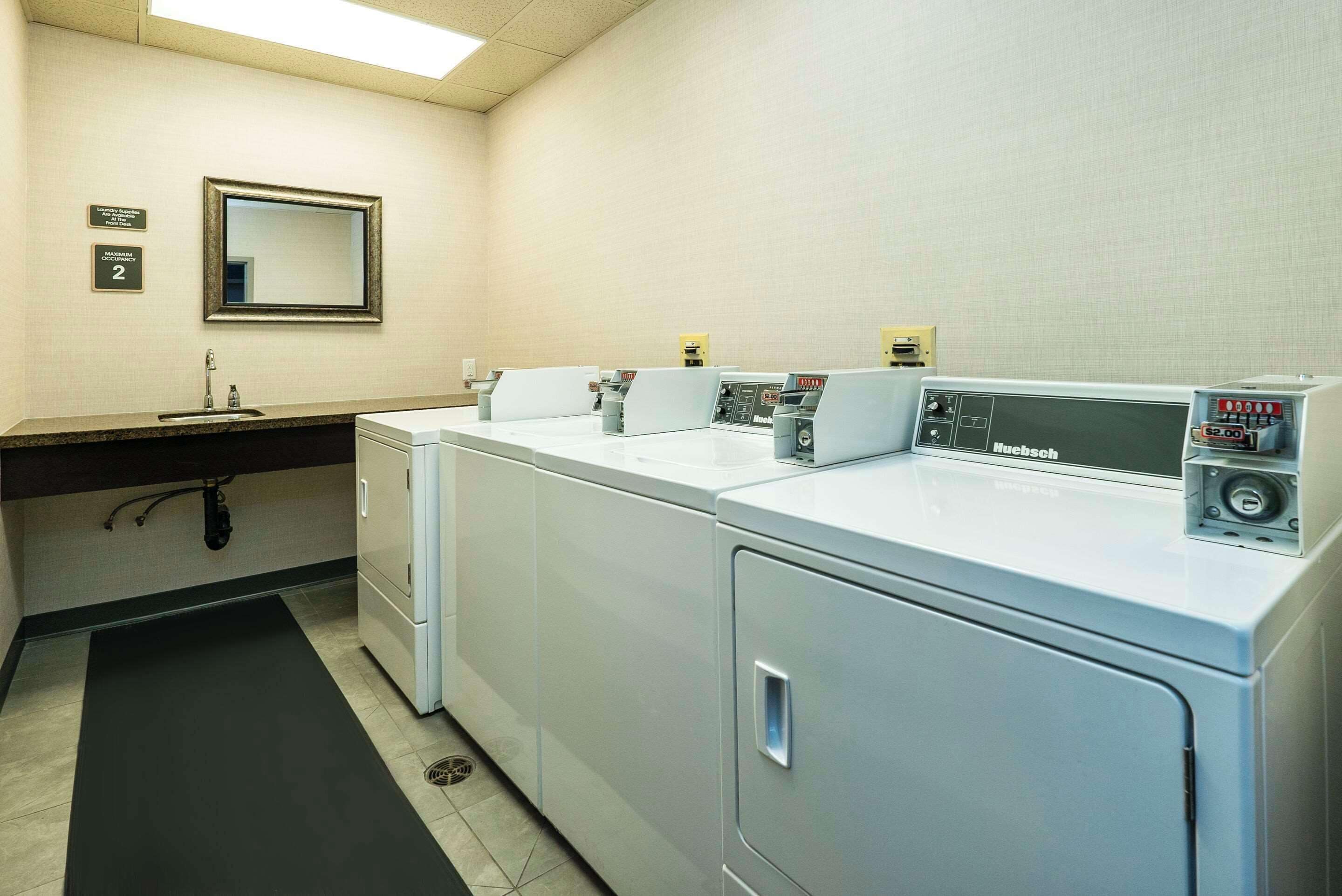 A laundry facility with a sink, mirror, and multiple washing machines.