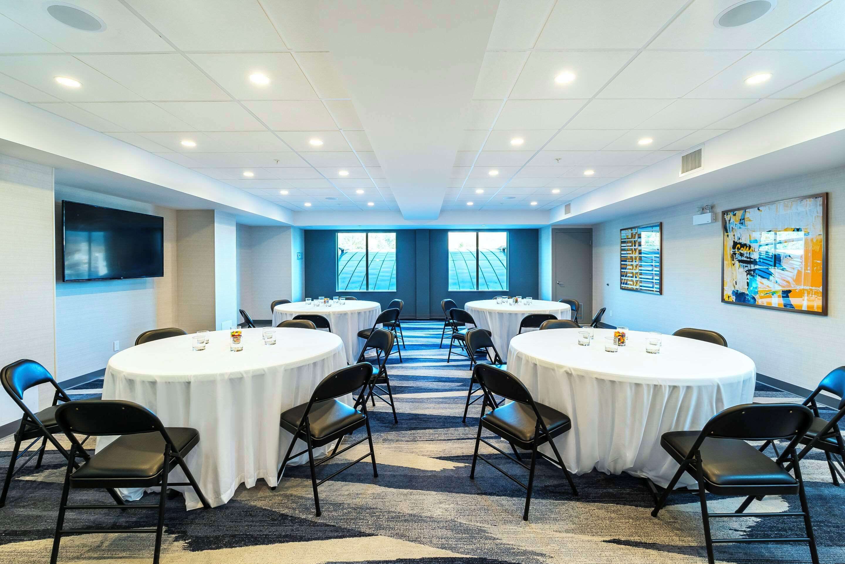 A conference room with round tables, black chairs, and a carpeted floor.
