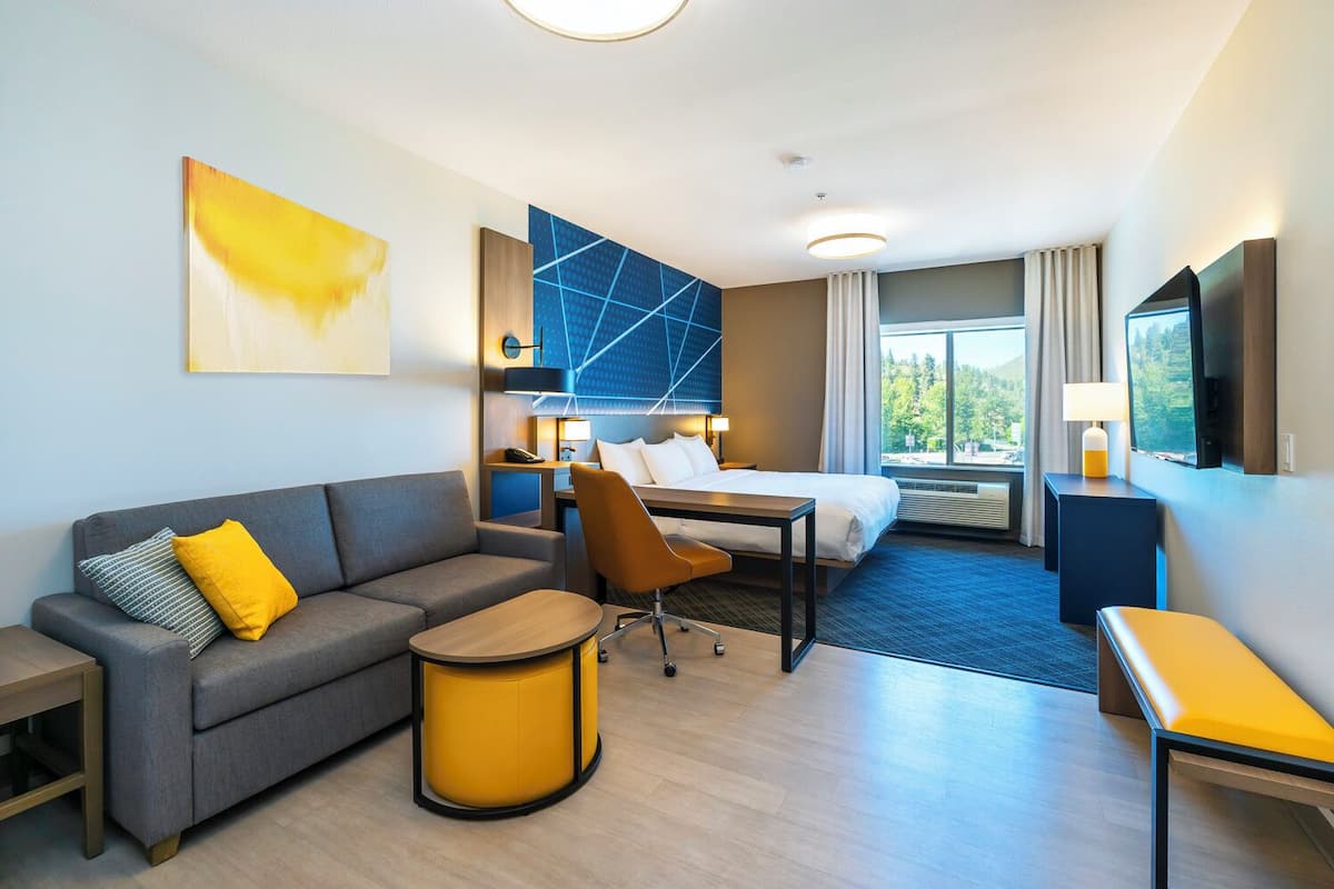A modern hotel room with a sofa, a small table, a desk, a bed, and a large window offering a view.