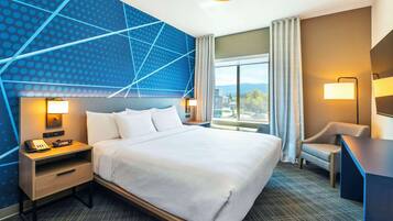 Une chambre d’hôtel avec un grand lit, un bureau, une chaise, une table de chevet avec un téléphone et un mur orné d’un motif géométrique.