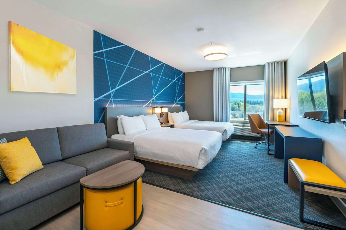 A hotel room with a sofa, two beds, a desk, a chair, and a TV.