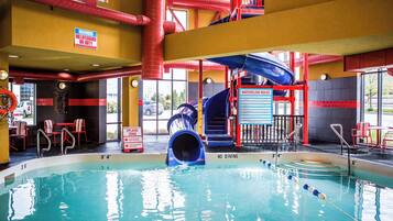 Una piscina interior con tobogán, sillas de salvavidas y un cartel de prohibición de clavados.