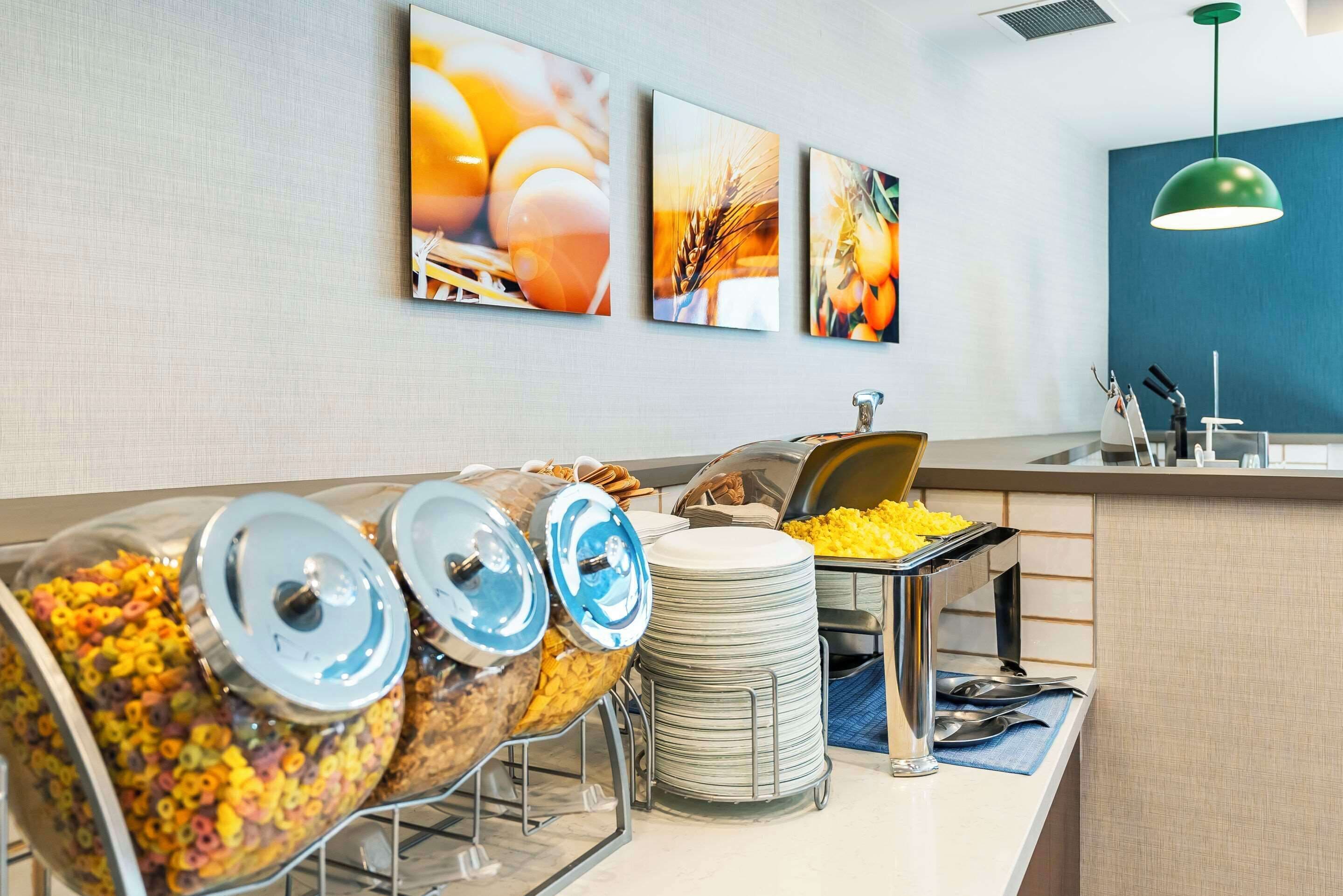 Disposición de bufé con cereales, barritas de cereales, una pila de platos y un dispensador de alimentos.