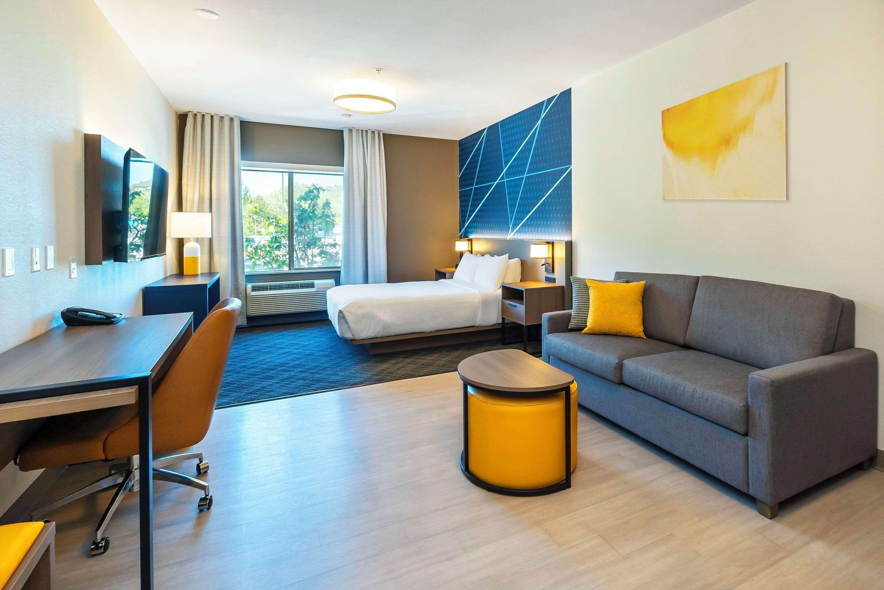 A modern hotel room with a bed, a sofa, a desk, and a TV.