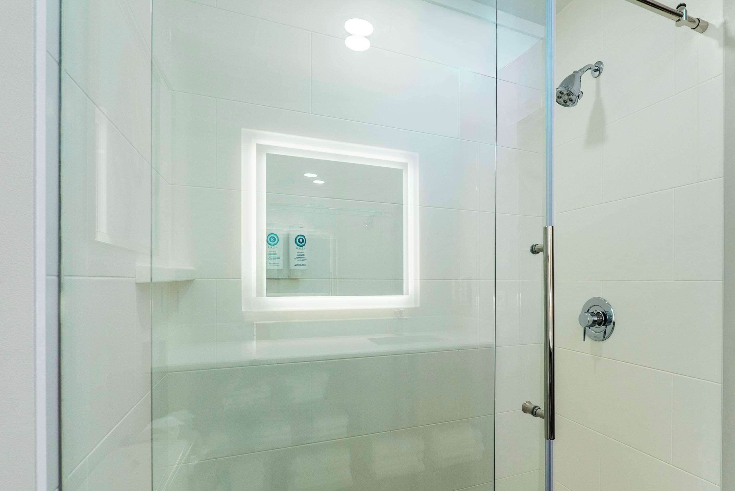 A glass-enclosed shower area with a glass door, a visible showerhead, and a control panel.