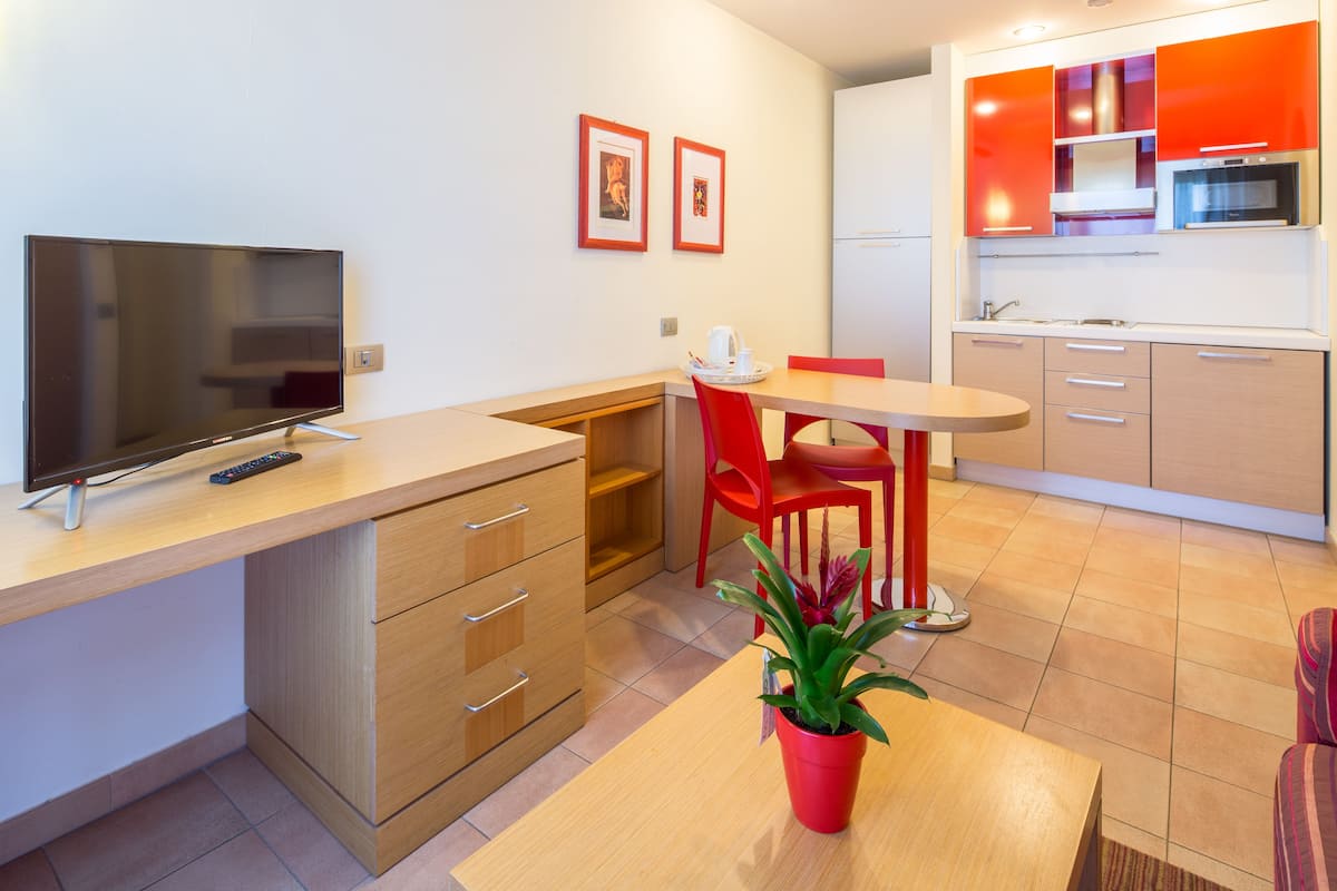A modern kitchen with a TV, red chairs, and a potted plant.