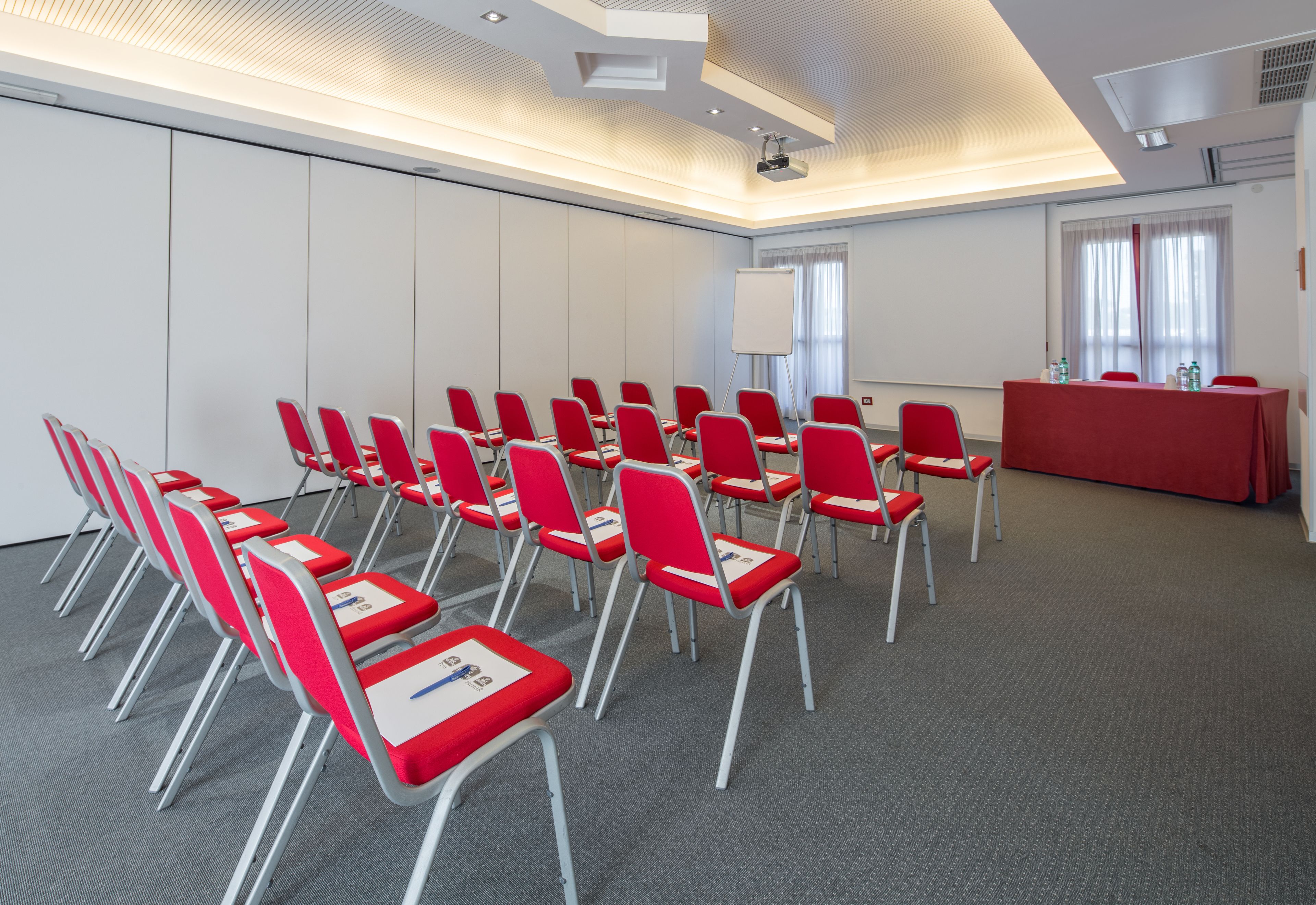 A conference room with rows of red chairs, a whiteboard, and a projector screen.