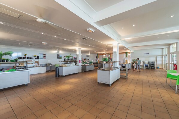 A spacious cafeteria with multiple serving stations, a clean tiled floor, and potted plants. - Belambra Clubs Montpezat - Le Verdon (Montagnac-Montpezat)