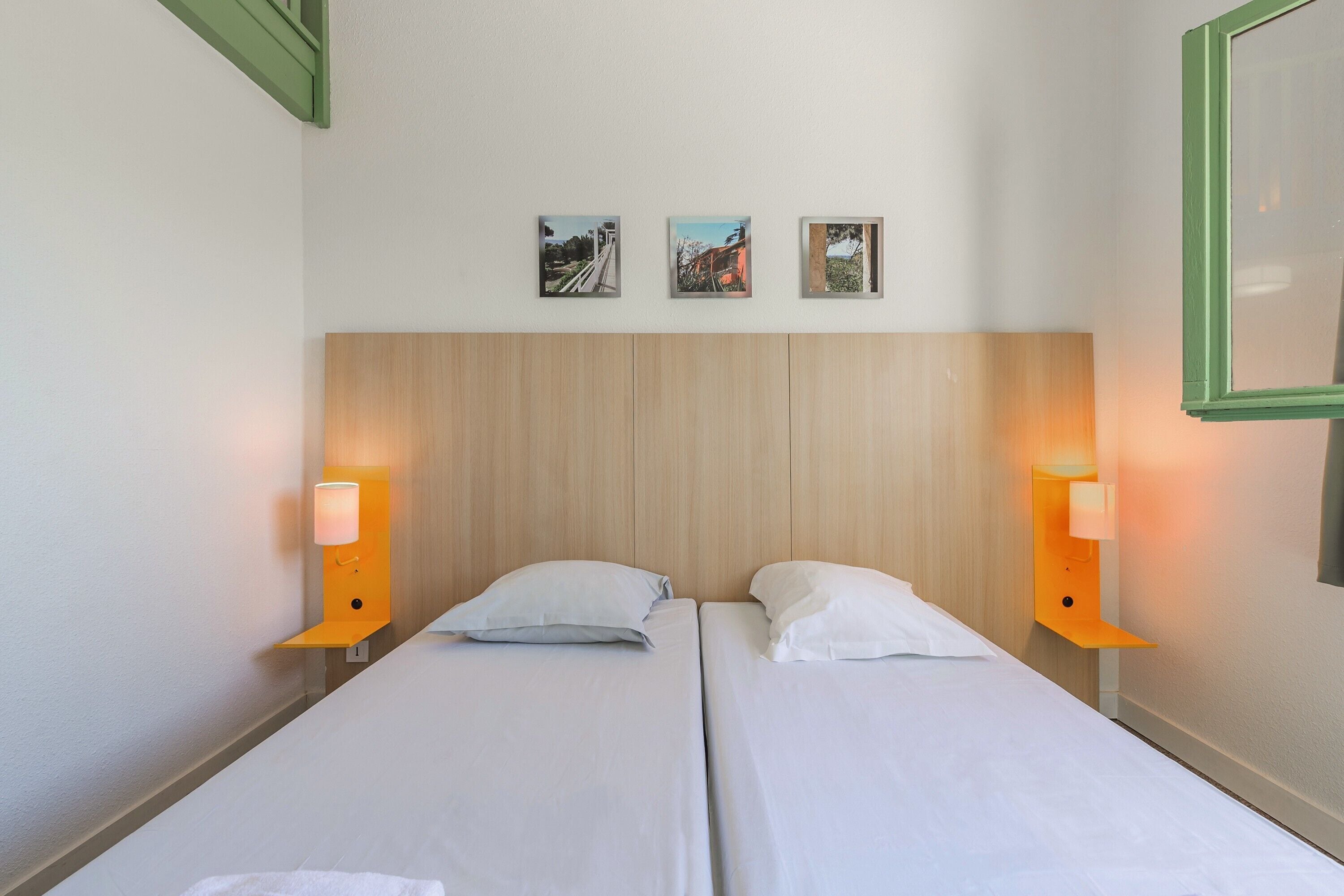 Ein Hotelzimmer mit zwei Betten, einem Holzkopfende, Wandbildern und Nachttischlampen.