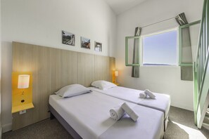 Une chambre d’hôtel avec deux lits, une tête de lit en bois, une fenêtre donnant sur un beau paysage et une lampe fixée au mur.