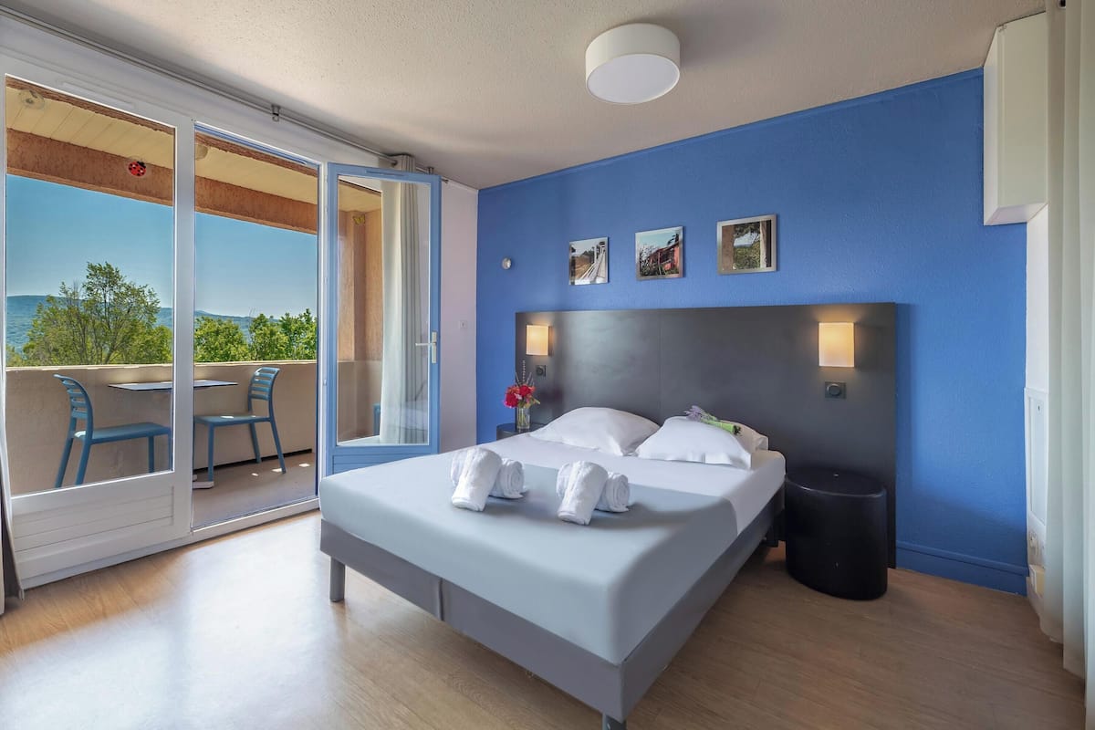 Ein Hotelzimmer mit Bett, Nachttisch, Fenster und Blick ins Freie.