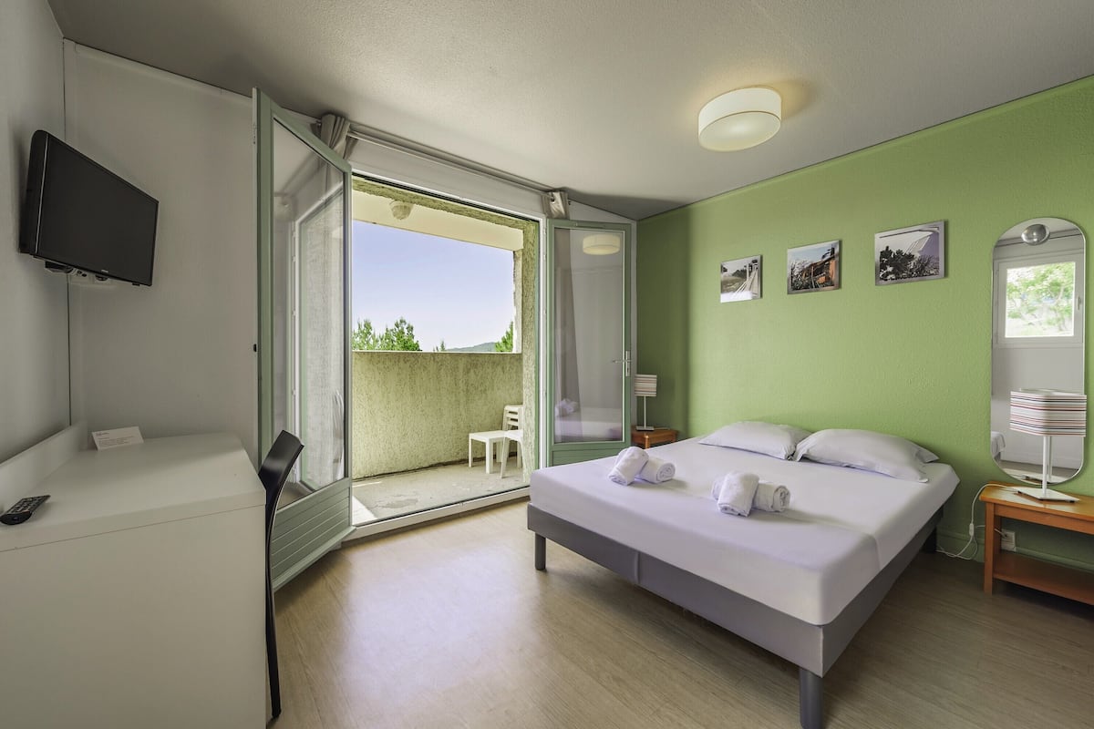 Ein Hotelzimmer mit Bett, Schreibtisch, Fernseher, Balkon und einer grünen Wand mit Bildern.
