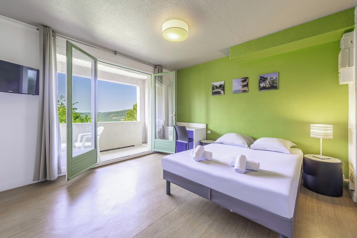 Ein Hotelzimmer mit Bett, Schreibtisch, Stuhl, Fernseher und einem Balkon mit Aussicht.