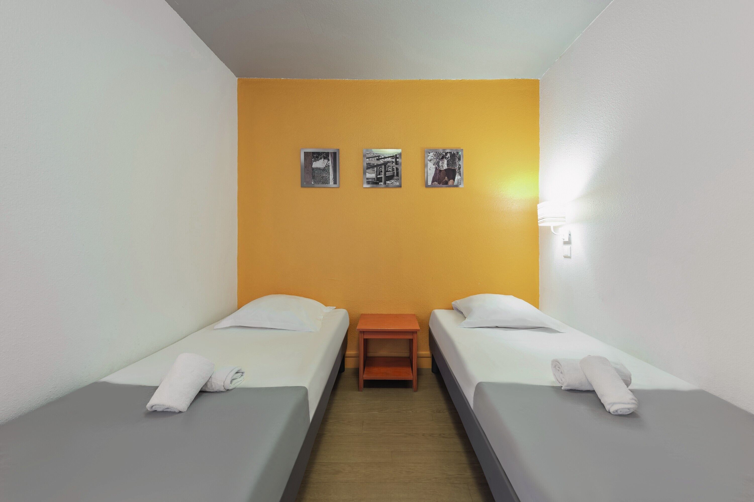 A room with two beds, a nightstand, and a wall with three framed pictures.