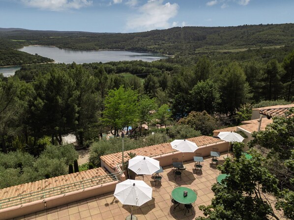 A terrace with outdoor seating, a view of a lake, and surrounding forested hills. - Belambra Clubs Montpezat - Le Verdon (Montagnac-Montpezat)