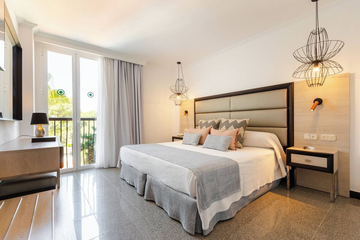 A modern bedroom with a large bed, a desk, a chair, and a balcony with a view.