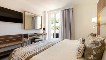 A hotel room with a bed, a desk, a chair, a mirror, and a view of the outdoors.