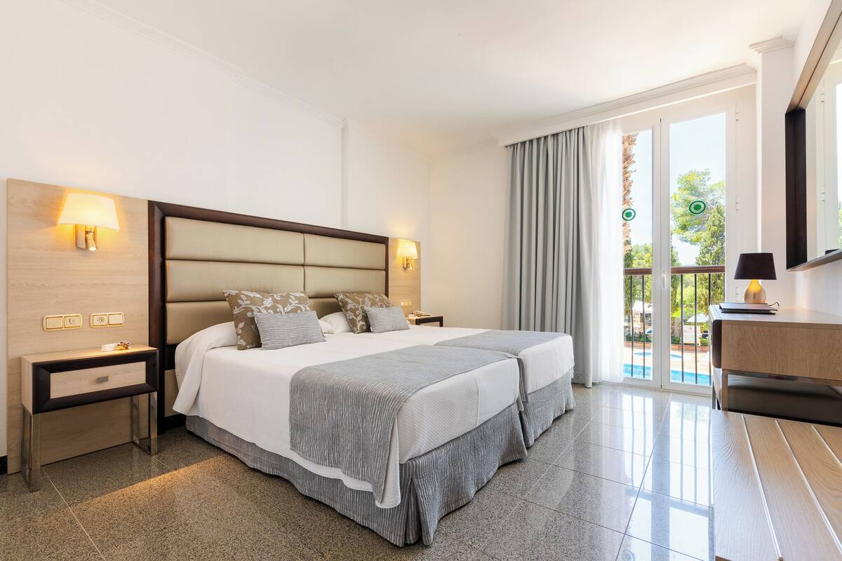 A hotel room with a large bed, two bedside tables with lamps, a wooden headboard, a balcony with a view, and a sliding glass door.