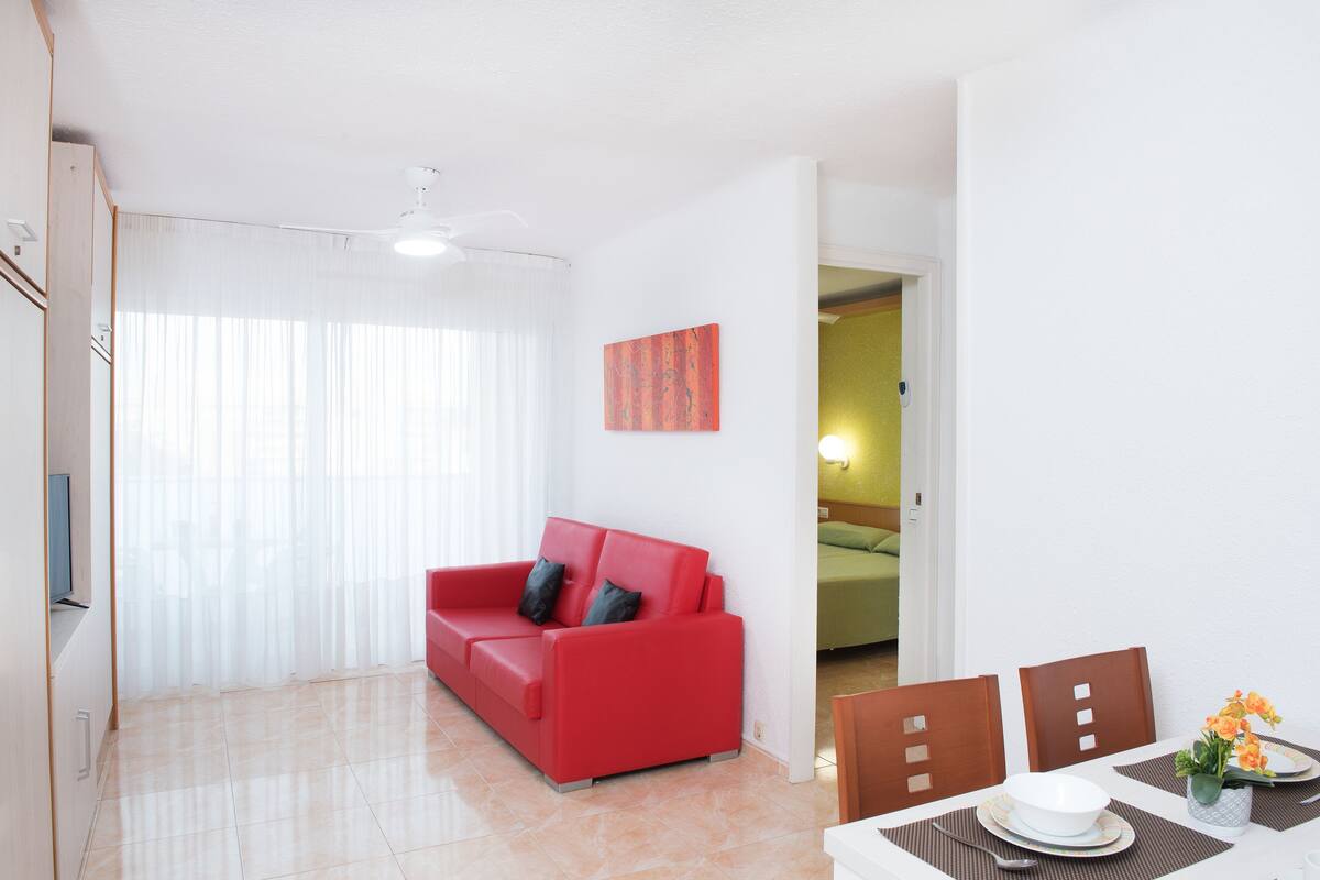 Una sala de estar moderna con un sofá rojo, una mesa de comedor con sillas y un ventilador de techo.