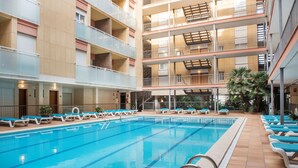 A multi-level indoor swimming pool with clear blue water, multiple lounge areas with blue chairs, and a tiled floor. - Apartamentos Costa d'Or (Calafell)