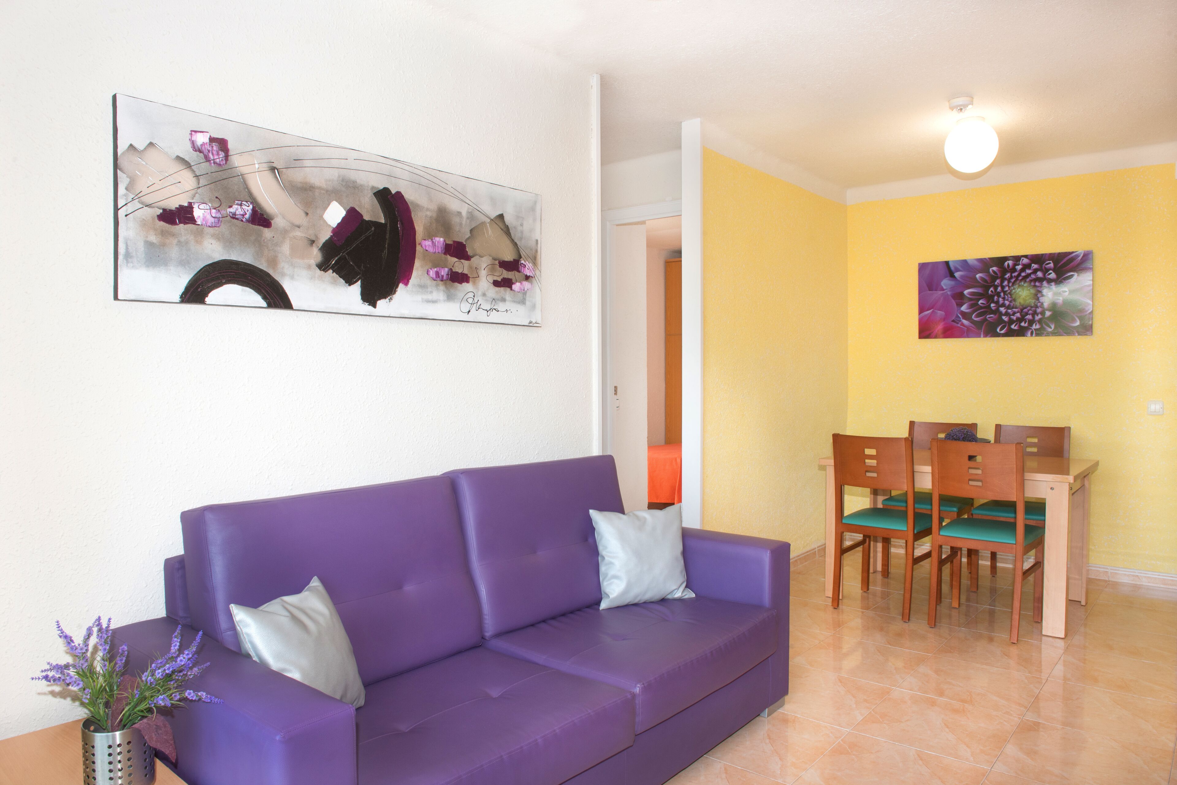 Un canapé violet avec un coussin, une table à manger avec des chaises et un tableau accroché au mur.