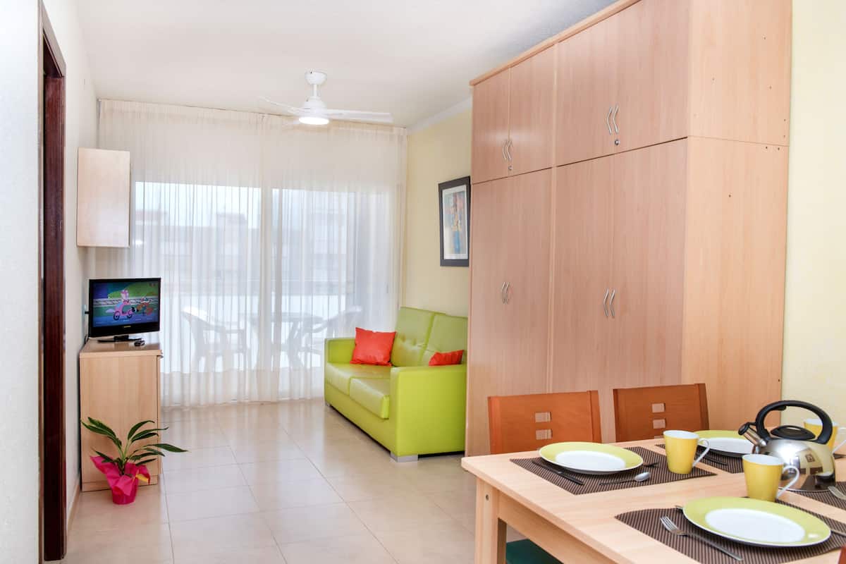 Una sala de estar moderna con televisor, un sofá verde, una mesa de comedor para dos personas y un aparador de madera.