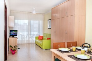 A modern living room with a television, a green sofa, a dining table set for two, and a wooden cabinet.