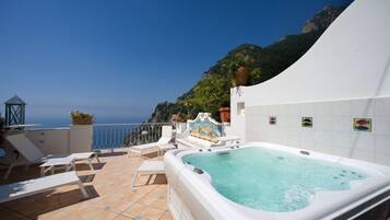 A rooftop terrace with a hot tub, lounge chairs, and a scenic ocean view.