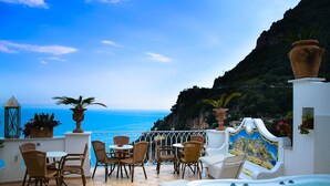 A terrace with wicker chairs and a table, overlooking a coastal view with a cliff and a clear sky. - Palazzo Marzoli Resort (Positano)