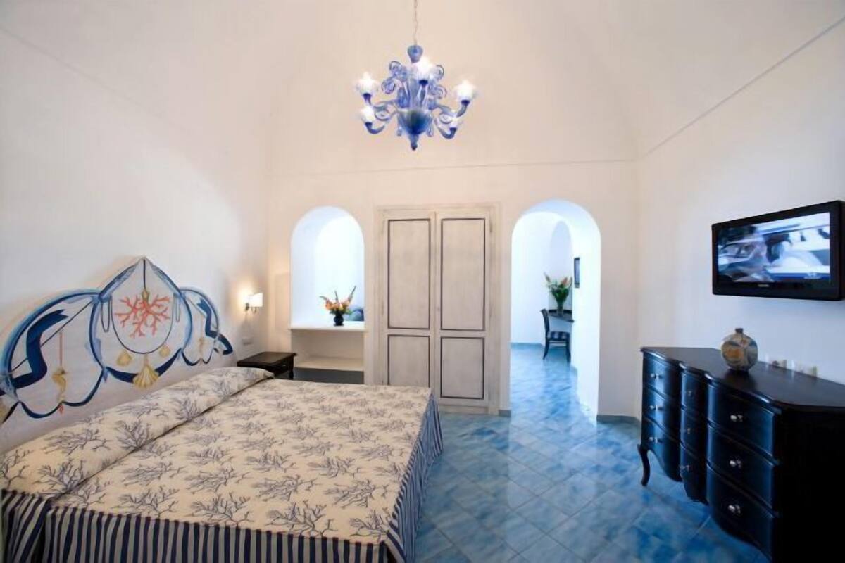 A bedroom with a bed, a chandelier, a TV, and a dresser.