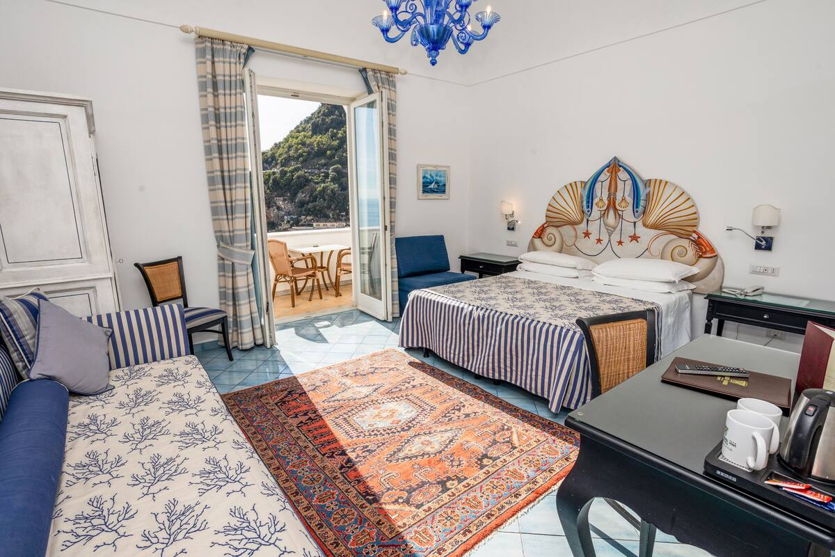 A bedroom with a bed, a sofa, a desk, and a view of a mountainous landscape.