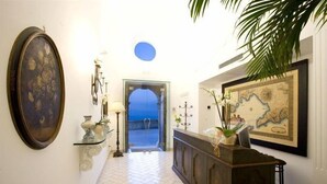 A hallway with a tiled floor, a large framed painting, a map, and a plant. - Palazzo Marzoli Resort (Positano)