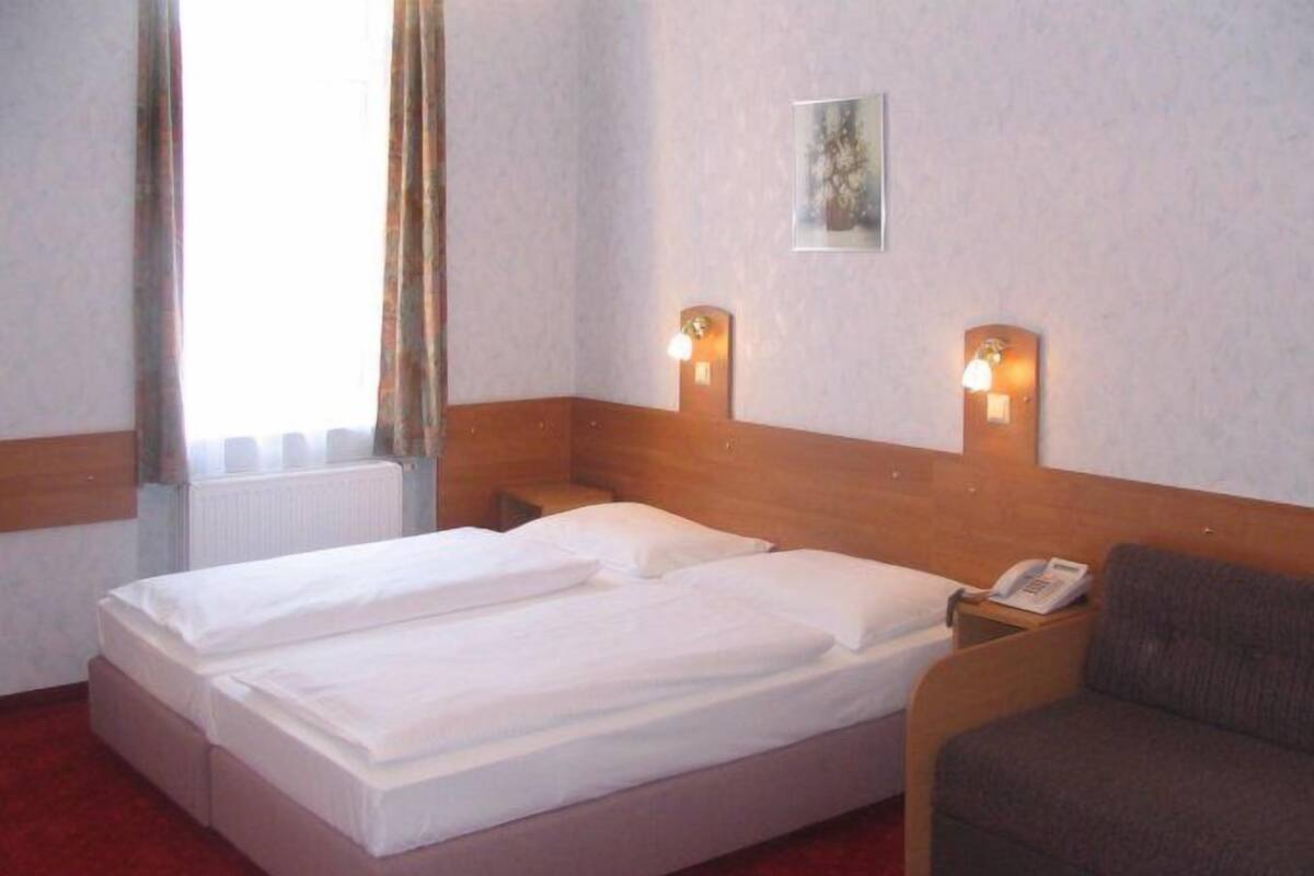 A hotel room with a double bed, a bedside table with a phone, and a sofa.