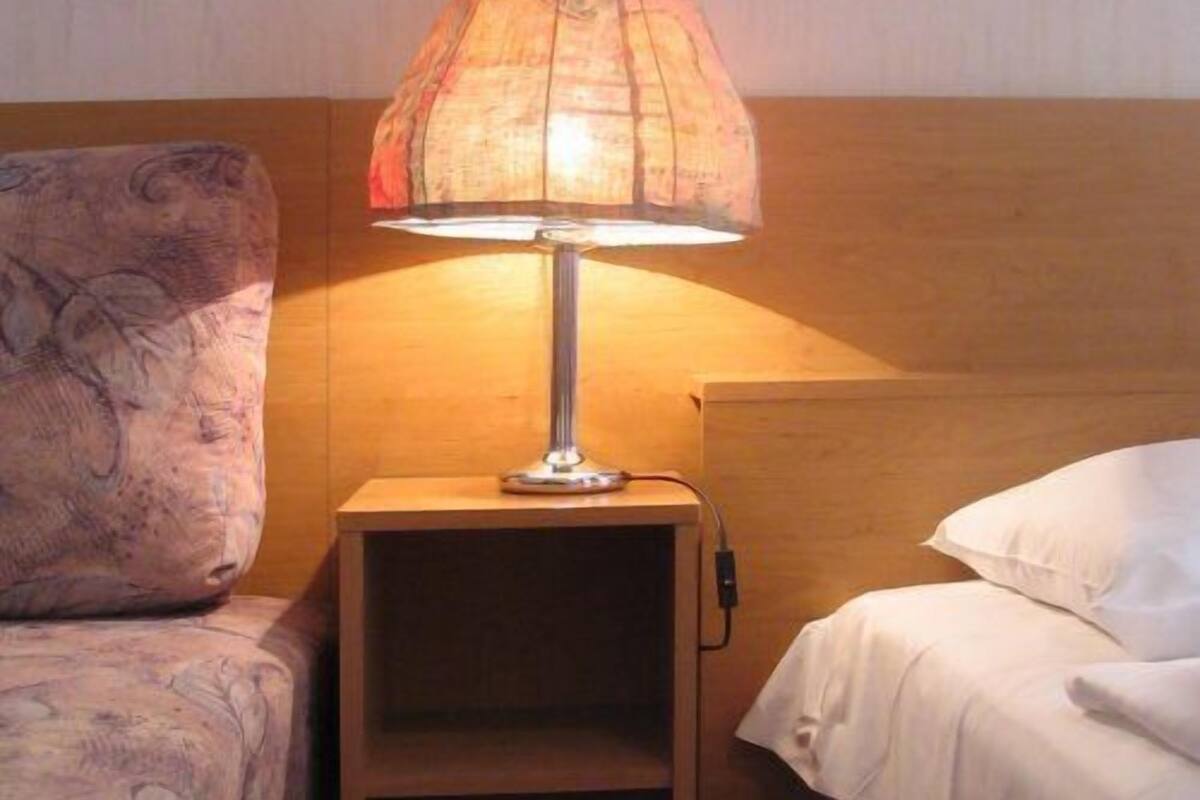 A small, cozy hotel room with a single bed, a nightstand with a lamp, and a patterned pillow.