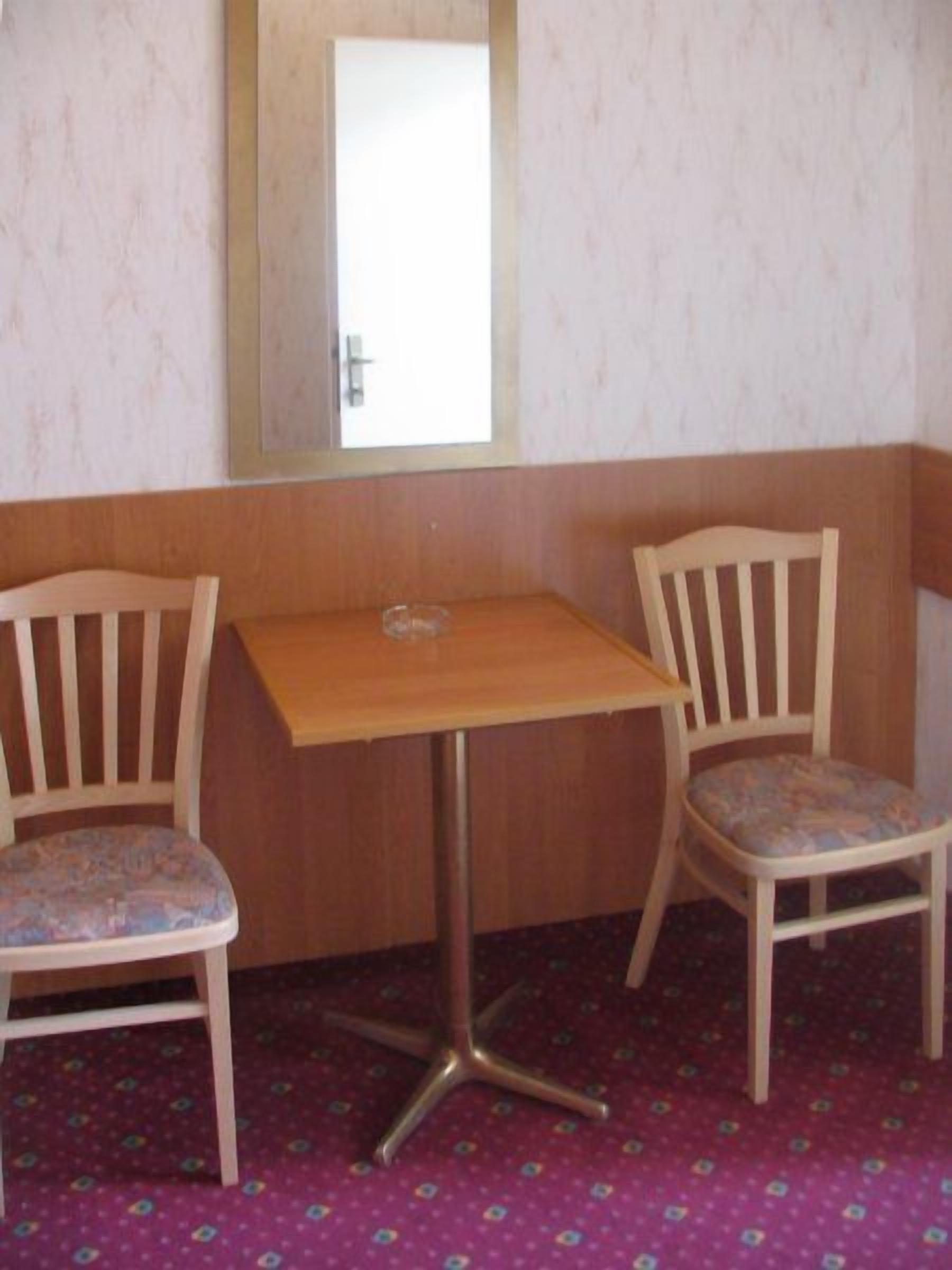 Una habitación pequeña con una mesa de madera y dos sillas, una ventana con un acceso, y alfombra estampada.