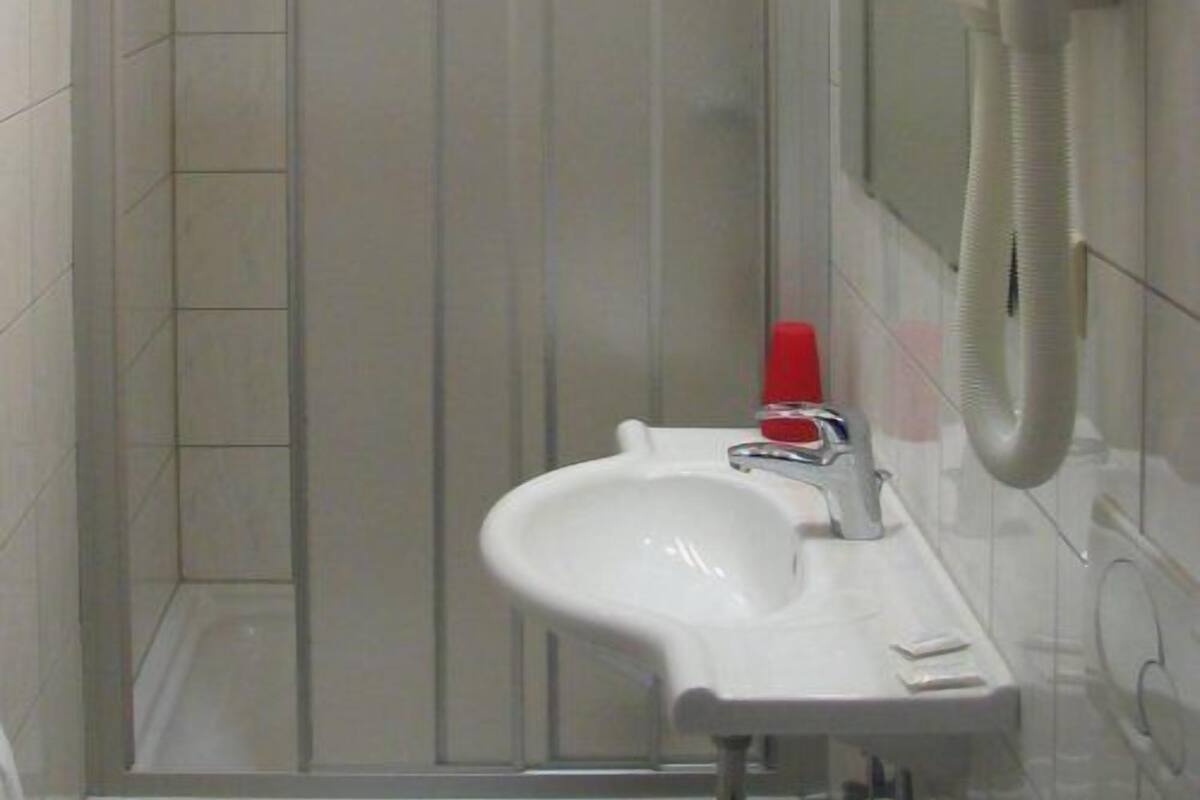 A bathroom with a glass shower enclosure, a white sink, and a telephone mounted on the wall.