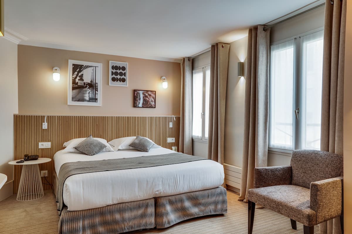A hotel room with a large bed, a chair, a bedside table, and a wall-mounted light.