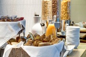 Un bufé con diversas opciones para el desayuno, incluyendo pasteles y un vaso de jugo de naranja.