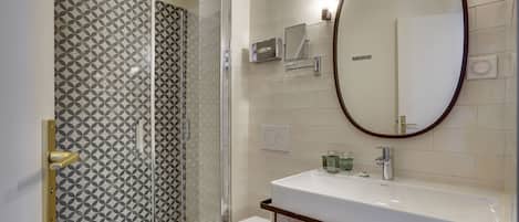 Een moderne badkamer met een douchecabine van glas, een wit toilet en een grote spiegel boven een witte wastafel.