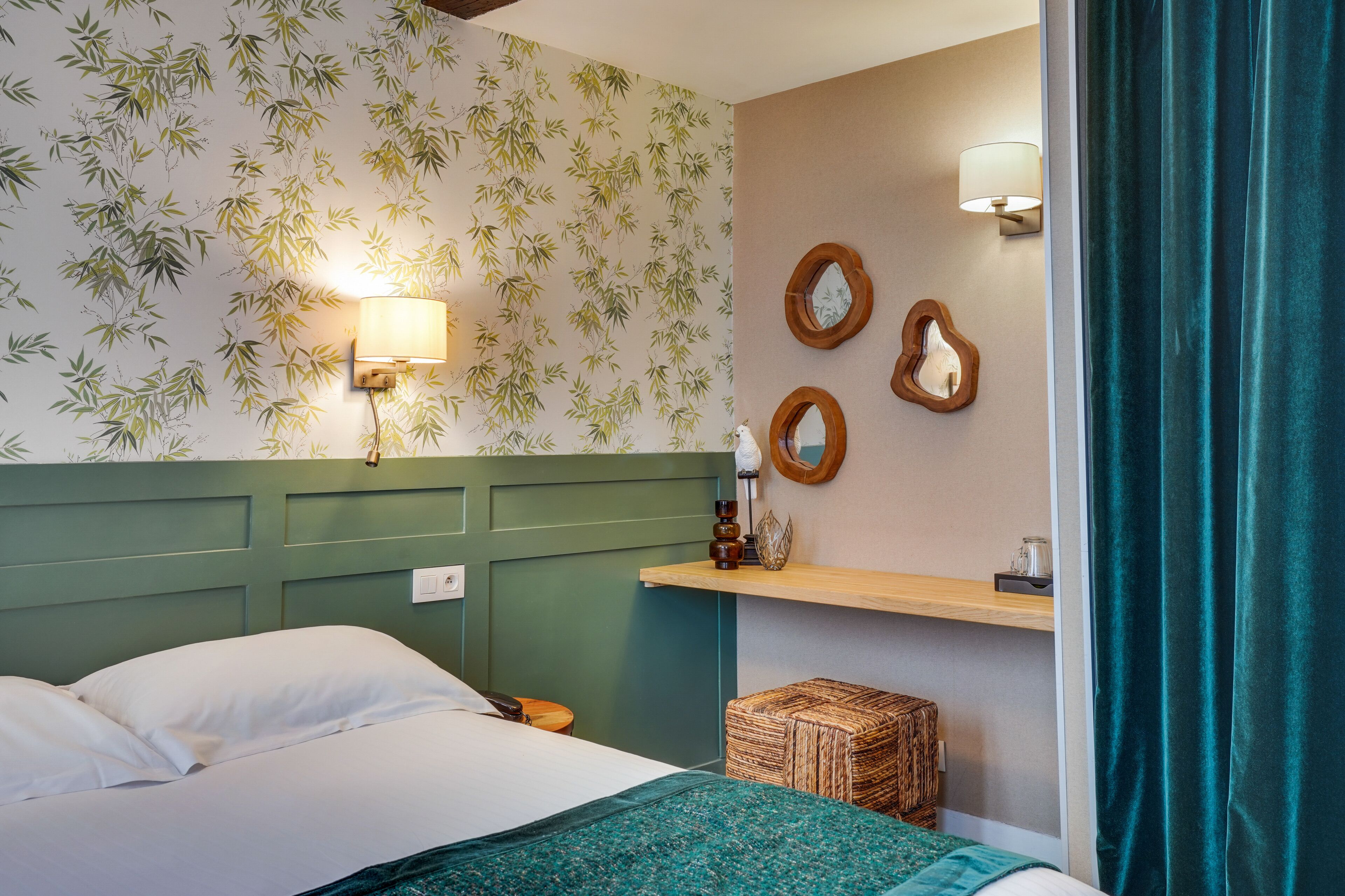 Camera d'albergo con un letto, una lampada a parete, uno specchio e una mensola con oggetti decorativi.