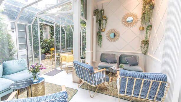 A conservatory with a glass ceiling, furnished with blue and grey sofas, patterned chairs, and a small table. - Hotel Passy Eiffel (Paris)