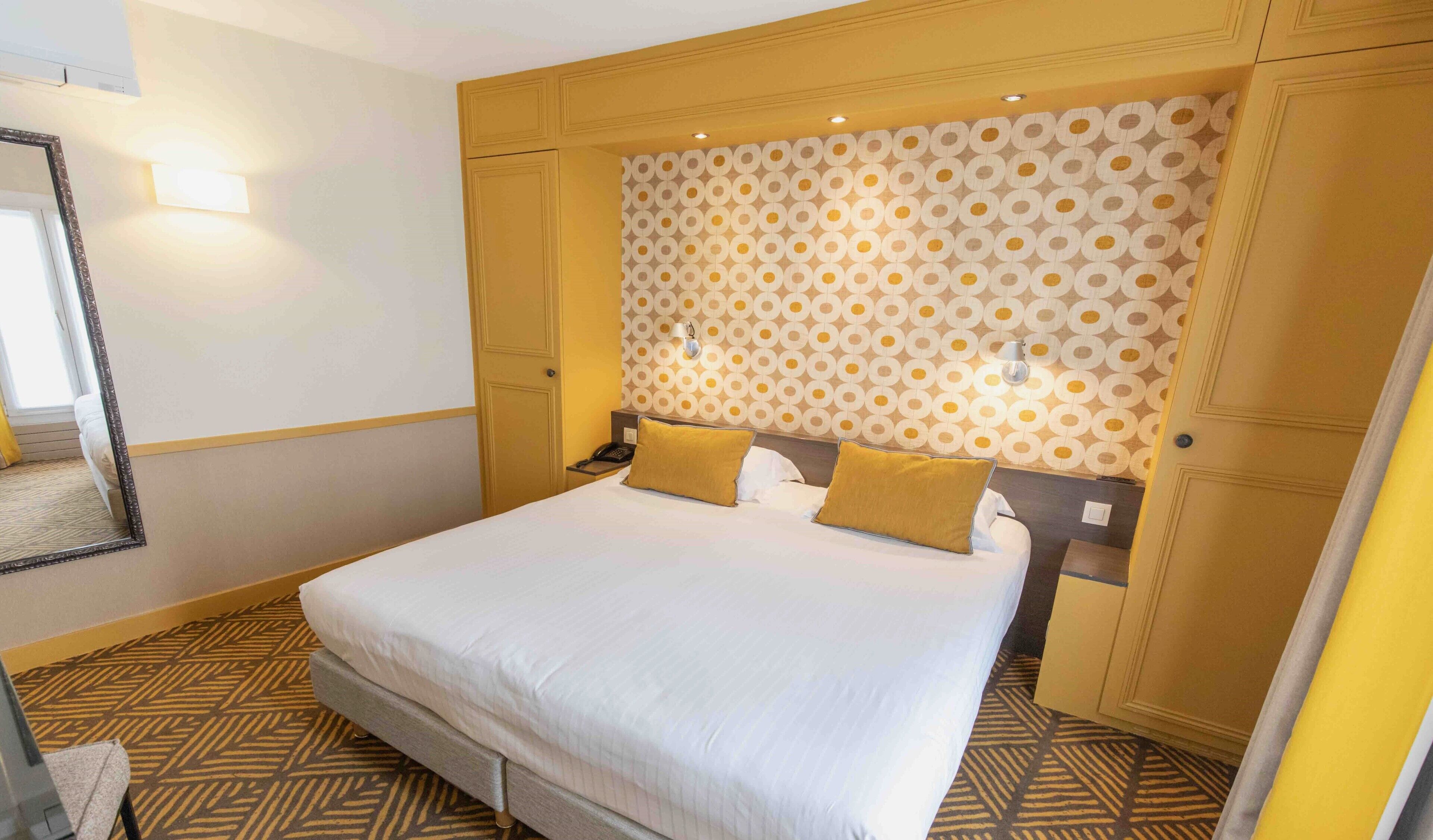 A hotel room with a large bed, a patterned headboard, and a mirror.